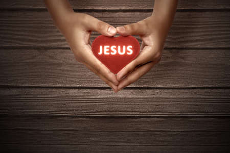 Human hands showing red heart with Jesus text with wooden background