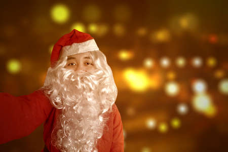 Asian man in Santa costume taking a selfie with a blurred light background. Merry Christmasの写真素材