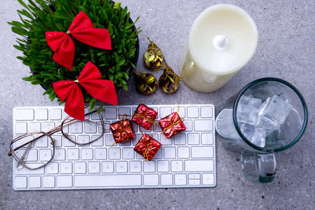 Close up view of millet grass plant in the pot with Christmas decoration, empty glass with an ice cube, and the keyboard on the deskの写真素材