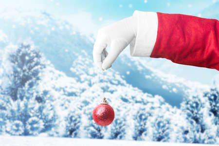 Santa Claus hand holding Christmas ball with snowfall background. Merry Christmasの写真素材