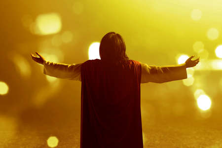 Rear view of Jesus Christ raised hands and praying to god with blurred light backgroundの写真素材