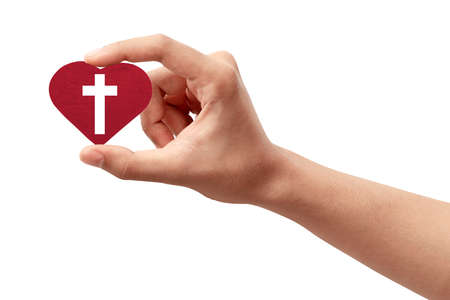 Human hand holding a red heart with a Christian cross isolated over white backgroundの写真素材
