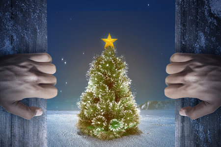 Hand opening wooden door with a Christmas tree with colorful ornament on the snow with snowfall backgroundの写真素材