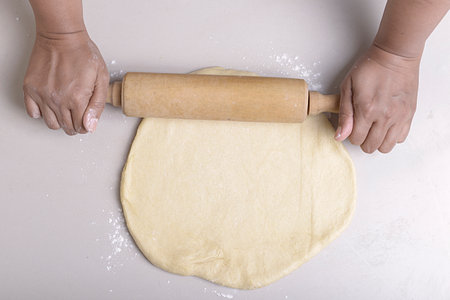 Hands making dough with a rolling pin on the table