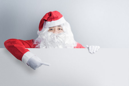 Asian man in Santa costume showing an empty board with a white wall background. Empty board for copy spaceの写真素材