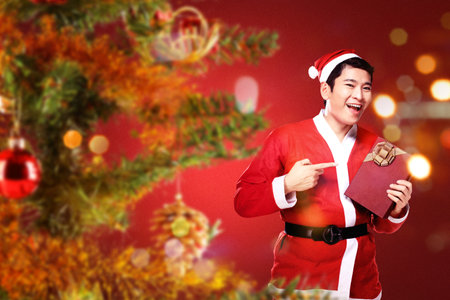 Asian man in Santa costume holding gift box with blurred light background. Merry Christmasの写真素材