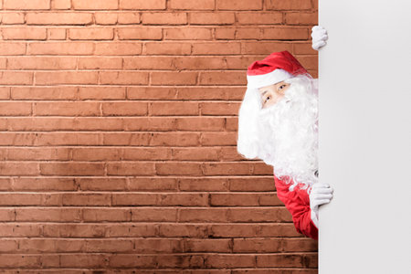 Asian man in Santa costume showing an empty board with a brick wall background. Empty board for copy spaceの写真素材