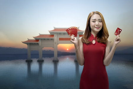 Asian Chinese woman in a cheongsam dress holding a credit card and red envelopes. Happy Chinese New Yearの写真素材