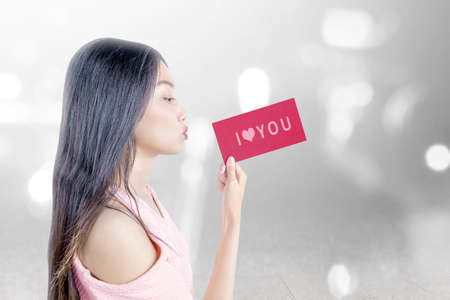 Asian woman holding a red paper with I Love You text with blurred light background. Valentines dayの写真素材