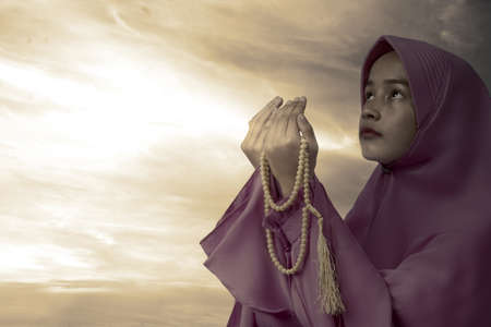 Asian Muslim woman in veil praying with prayer beads on her hands with a dramatic sky background