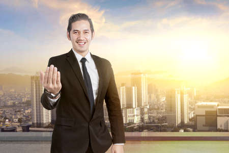 Asian businessman with hand gesture on the rooftop with skyscrapers backgroundの写真素材