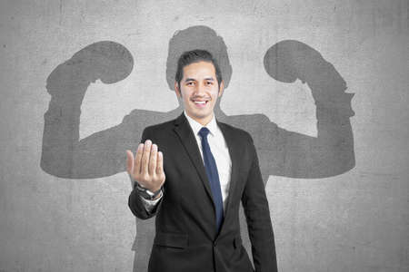 Asian businessman with hand gesture and muscular shadow on the wallの写真素材