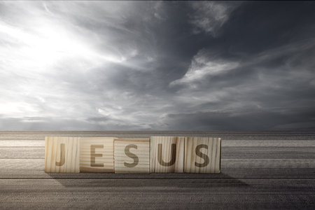 Wooden cube with Jesus text on wooden table with a dramatic sky backgroundの写真素材