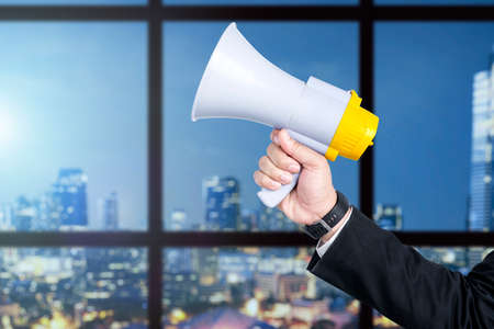 Businessman hand holding megaphone with office building background