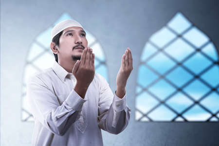 Asian Muslim man standing while raised hands and praying on the mosque