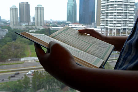 Muslim man holding open the Quran on his hands with cityscapes background