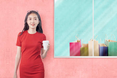 Asian woman holding a coffee cup with shopping bags on the display storeの写真素材