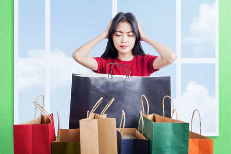 Asian woman shocked with so many shopping bags with green wall backgroundの写真素材