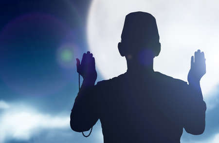 Silhouette of Muslim man praying with prayer beads on his hands with a night scene backgroundの写真素材