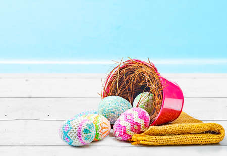 Colorful easter eggs spilled from the nest in a red bucket with fabric on a wooden table. Happy...