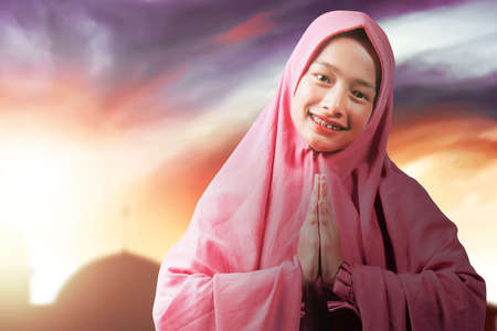 Asian Muslim woman in veil with greeting gesture with dramatic sky backgroundの写真素材