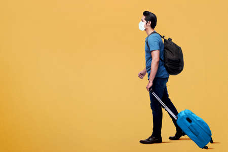 Asian man in the face mask with backpack and suitcase with a colored background. Traveling in the new normalの写真素材