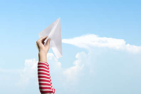 Girl hands holding paper plane ready to launch with a blue sky background. World Children Dayの写真素材