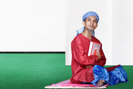 Asian Muslim man sitting and holding the Quran on the mosque