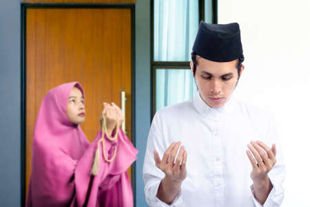 Asian Muslim couple standing while raised hands and praying together at homeの写真素材