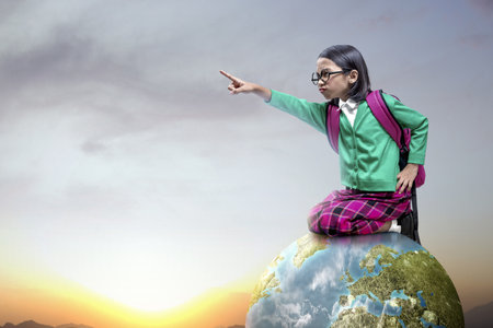 Asian little girl with glasses and backpack sitting and pointing something on the earth. World Children Dayの写真素材
