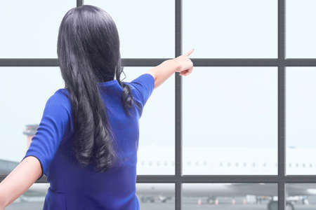 Rear view of Asian woman pointing something on the airport terminal. Traveling in the new normalの写真素材