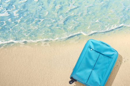 Blue suitcase with water waves on the sandy beachの写真素材