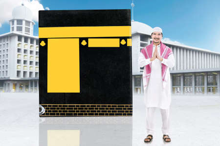 Asian Muslim man standing with greetings gesture with Kaaba background