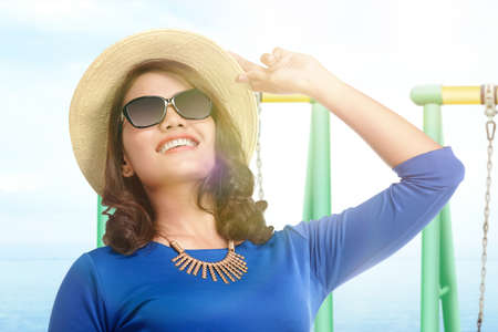Asian woman standing with hat and sunglasses on the beach with blue sky background