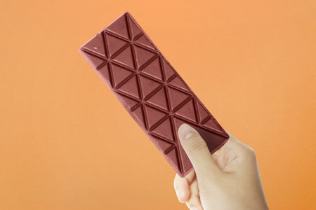 Human hand holding the chocolate bar with colored background