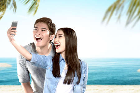 Asian couples making a selfie with a funny face on the beach with blue sky background
