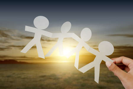 Hand holding white people paper holding hands with sunset scene background. World Population Day...