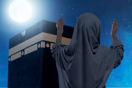 Rear view of Asian Muslim little girl in a veil standing and raised hands praying in front of the...