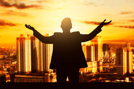 Silhouette of a businessman standing and raised hands with cityscapes background