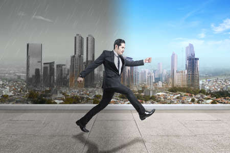 Asian businessman running to different climates with cityscapes backgroundの写真素材