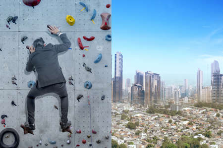 Asian businessman climb the rock climbing wall with blue sky background