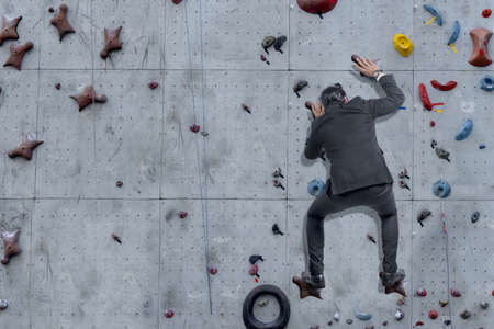 Asian businessman climb the rock climbing wall at outdoor