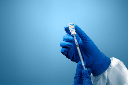 Health worker woman with a protective suit and gloves holding covid 19 vaccines with blue backgroundの写真素材