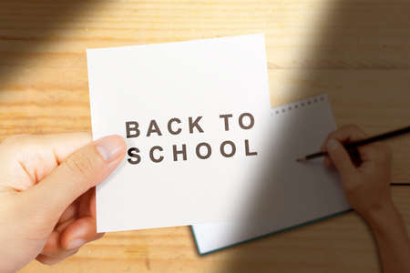 Hand holding paper with Back to school text with wooden background. Back to School conceptの写真素材