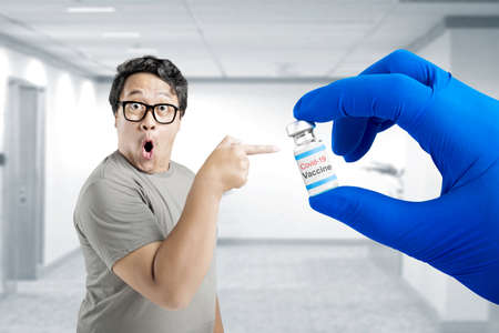 Asian man in eyeglasses pointing to health worker hand with gloves holding covid 19 vaccines for vaccinationの写真素材
