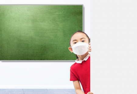Asian little girl wearing the mask standing beside the wall on the classroomの写真素材