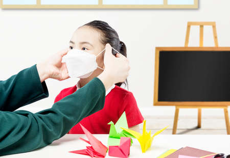 Mother hand putting the mask on her daughter in the classroom