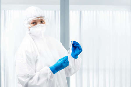 Health worker woman with a protective suit and gloves holding covid 19 vaccines on the hospitalの写真素材
