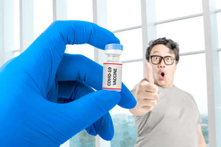 Asian man in eyeglasses showing thumb up with health worker hand with gloves holding  vaccines for...
