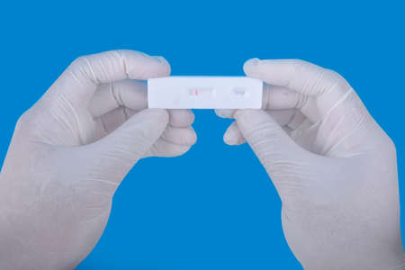 Health worker hand with protective gloves holding covid-19 antigen test kit with colored background